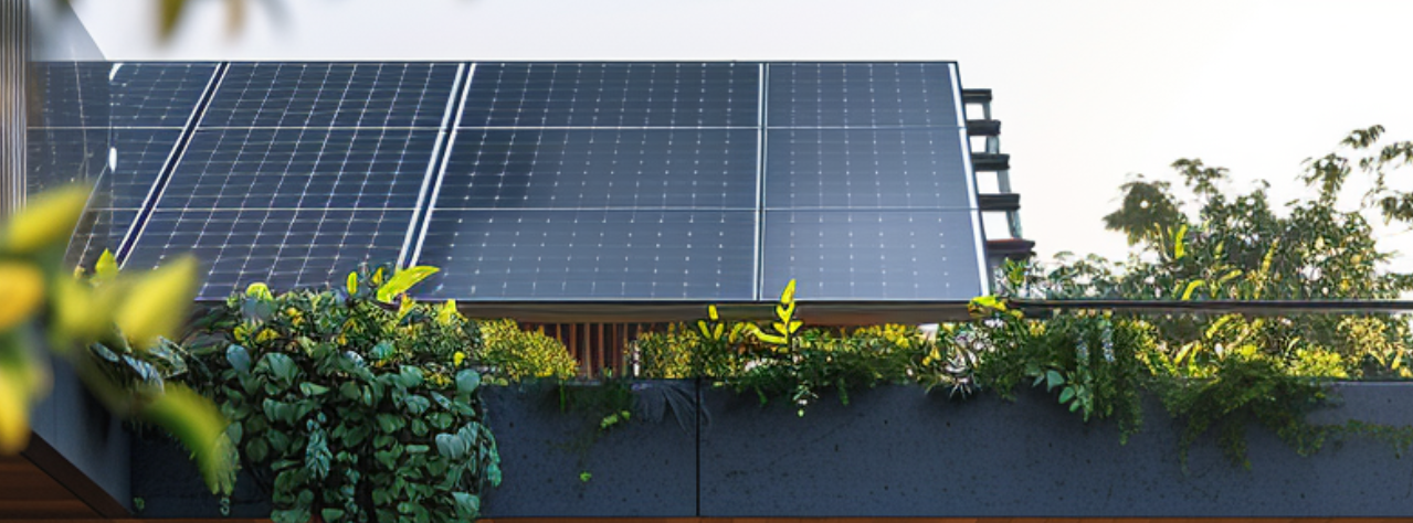 Umgeben von üppigem Grün im Garten, fängt ein imposantes schwarzes Solarpanel auf dem Dach das Sonnenlicht ein und versorgt das Zuhause mit unaufhörlicher, sauberer Energie – ein wertvoller Beitrag zum nachhaltigen Leben und zum Schutz der Umwelt.